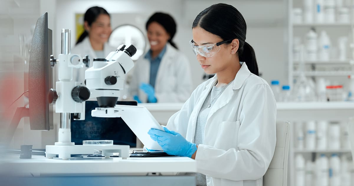 Scientist, study and woman with tablet by microscope for medical research, pathogen and development. Science, pharmaceutical and biotech with experiment for Mpox vaccine, innovation and epidemiology - LabLynx