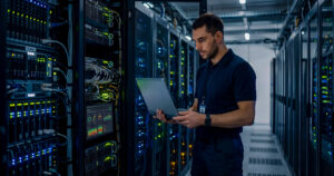 IT technician in a data center using a laptop to monitor server racks